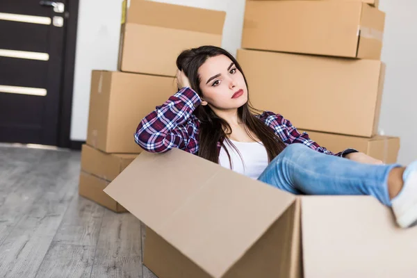 Ung trött kvinna som sitter inuti en låda bland en bunt flyttlådor — Stockfoto