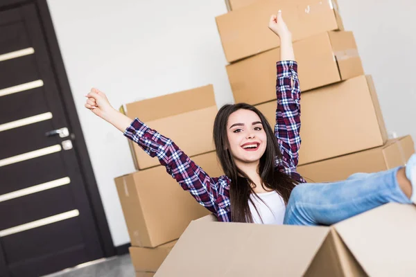 Glada kvinna sitter inuti en kartong medan packning flyttar till nytt hem — Stockfoto