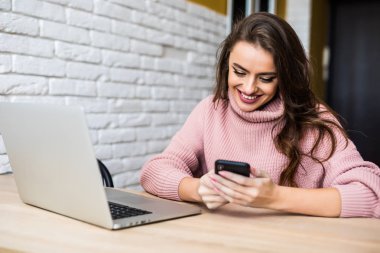 Güzel gülümseyen kadın masasında görmek dizüstü ev telefonunu kullanarak