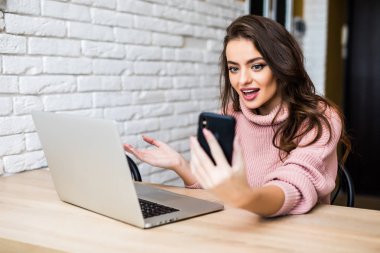 Güzel genç kız rahat kıyafetler içinde bir akıllı telefon ve bir dizüstü bilgisayar kullanarak ve evde masanda tablo sırasında gülümseyen