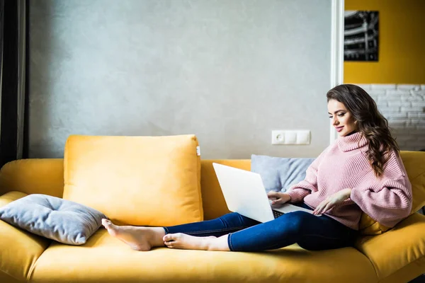 Beautiful smiling woman lying on the sofa with laptop — Stock Photo, Image