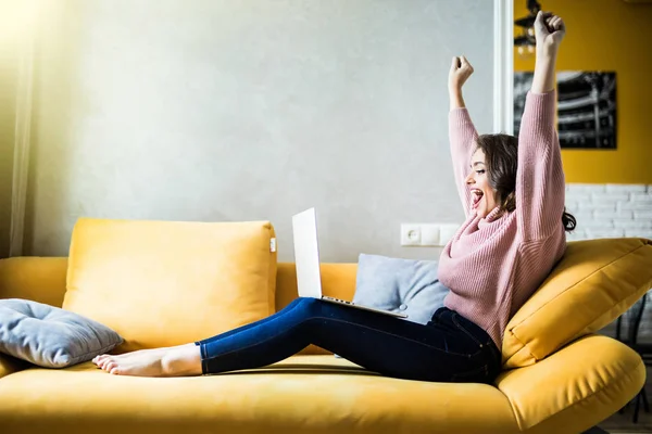 Pretty young woman using a laptop while raising hand and sitting on the couch — Stock Photo, Image