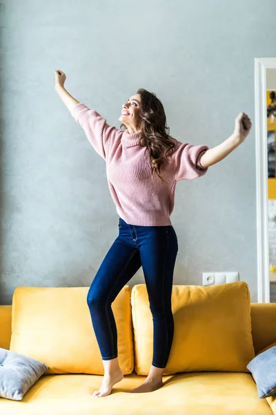 Beautiful woman jumping over the sofa at home — Stock Photo, Image