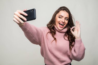 Selfie smartphone yapma ve iyi jest izole gri bir arka plan üzerinde gösterilen gülümseyen kız