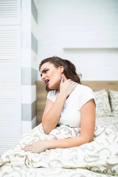 Jeune femme assise sur le lit avec douleur dans le cou à la maison — Photo