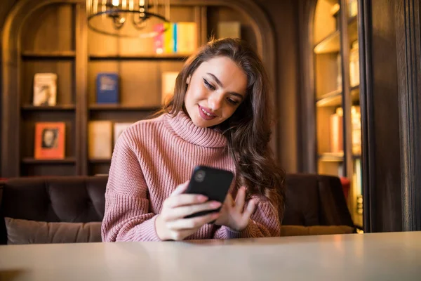 Woman typing write message on smart phone in a modern cafe. Young pretty girl sitting at a table with coffee or cappuccino using mobile phone. — Stock Photo, Image