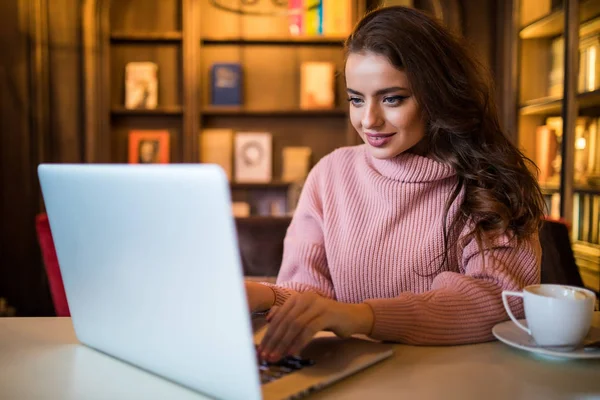 Beautiful young woman using laptop at cafe while drinking coffee at break time — Stock Photo, Image