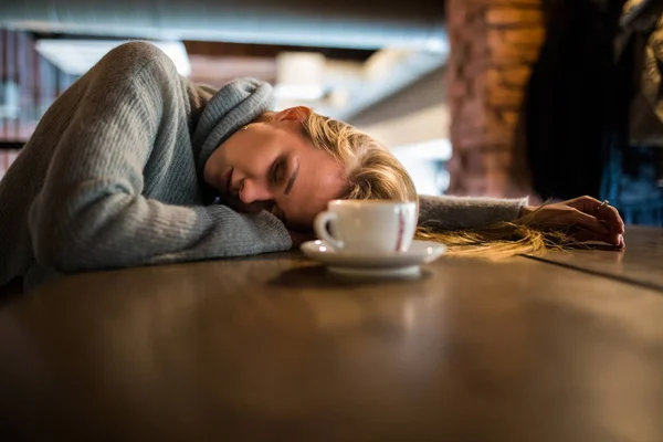 Belle jeune femme couchée sur les mains, assise à la table en bois à la cafétéria, boit du café. Concept de détente et de repos — Photo