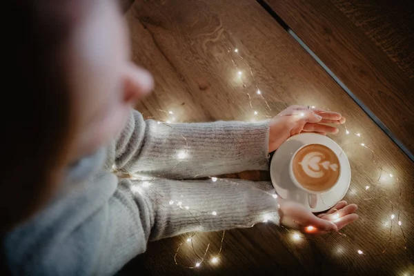 Girl holding coffee in hands over light bokeh background. Nice winter photo of hands with coffee cup with magic light.