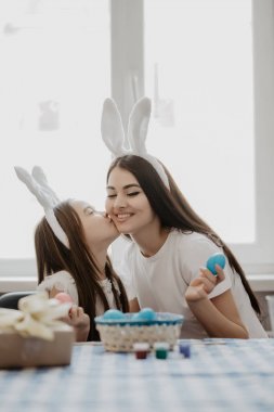 Anne ve kızı anne öpüşme kız oturan tavşan kulakları ev Paskalya hazırlanmasında, birlikte. Paskalya