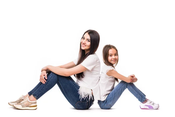 Маленькая девочка и ее старшая сестра сидят спиной к спине на белом фоне — стоковое фото