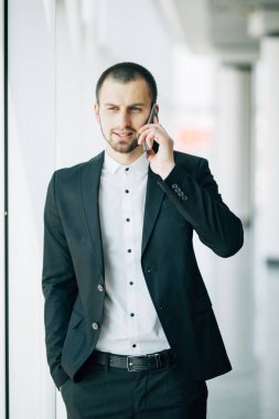 İş adamı Talking panoramik pencere işadamı içinde Coworking Merkezi Modern ofis iç önünde duran cep telefonu çağrı