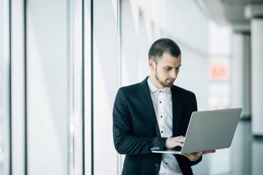 Genç işadamı ofiste ayakta eller içinde laptop üzerinde çalışıyor