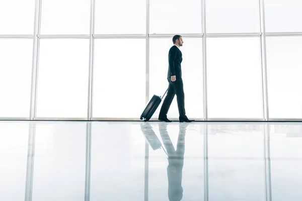 Jovem homem de negócios puxando mala no moderno terminal aeroportuário. Tipo viajante ou conceito de homem de negócios. Viagem de negócios — Fotografia de Stock