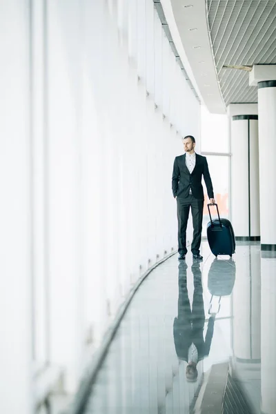 Pewny siebie młody człowiek patrzy lotu i zachód przez okno w Lotnisko stojący z walizką — Zdjęcie stockowe