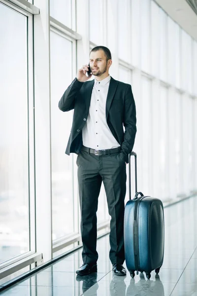 Ganzkörperporträt eines glücklichen Mannes, der mit Koffer und Handy im Terminal des Flughafens spaziert — Stockfoto