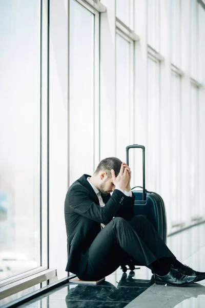 Homem de negócios sentado no aeroporto terminal no chão com atraso de voo mala, duas mãos tocar na cabeça, dor de cabeça, esperando viajar. Viagem de negócios — Fotografia de Stock