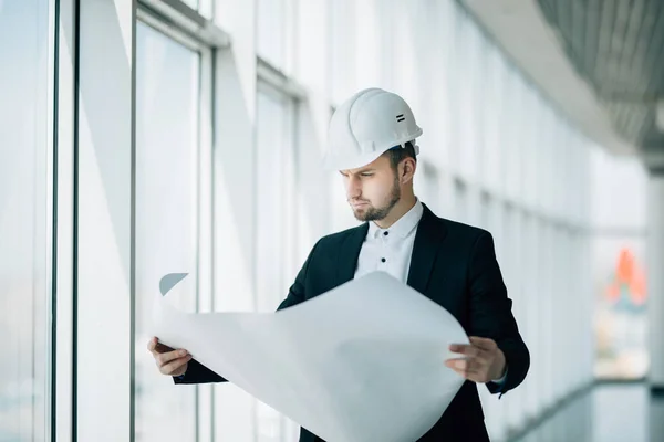 Porträtt av en leende manliga entreprenör ingenjör med hård hatt läsning blueprint på byggarbetsplats. — Stockfoto