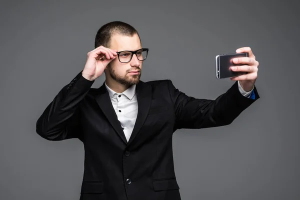Retrato de um empresário feliz vestido de terno e óculos enquanto está de pé e tomando uma selfie isolada sobre fundo cinza — Fotografia de Stock