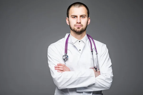 Retrato de médico masculino guapo serio con las manos cruzadas sobre fondo gris —  Fotos de Stock