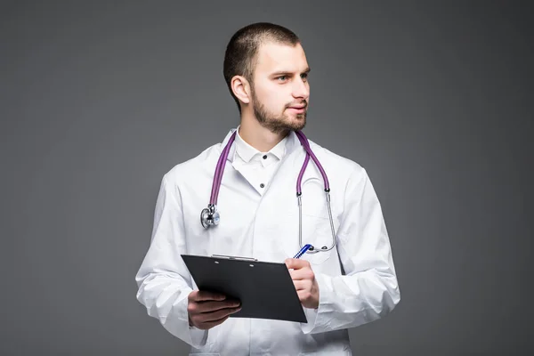 Portræt mandlige læge iført en medicinsk dragt hænge på stetoskop og holde udklipsholderen isoleret på grå. Læge koncept . - Stock-foto