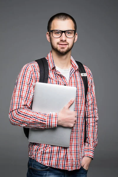 Handsome and young Male college student carrying bag on white background while holding college laptop isolated on gray