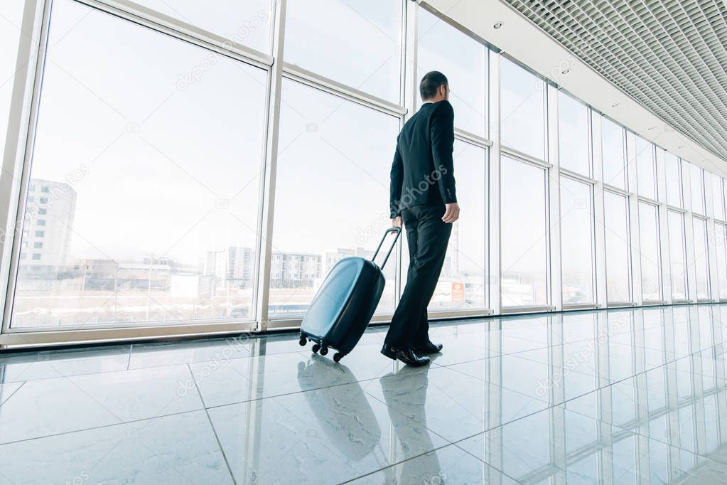 Young business man pulling suitcase in modern airport terminal. Travelling guy or businessman concept. Business trip