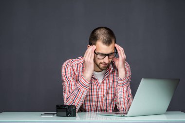 Dalgın hüzünlü adam masada laptop ile gri arka plan üzerinde oturuyor.