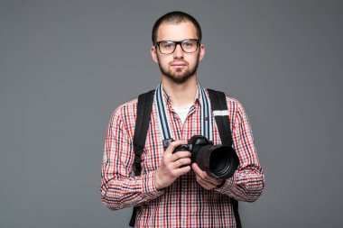 Gri arka plan üzerinde fotoğraf makinesi ile seyahat adam genç sakallı