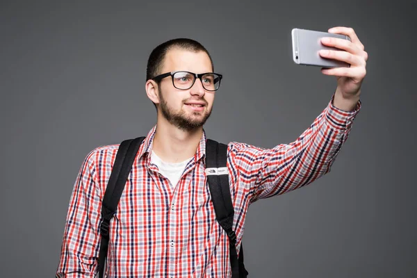 Szczęśliwy młody człowiek biorąc fotografii portret własny przez inteligentny telefon na szarym tle. — Zdjęcie stockowe