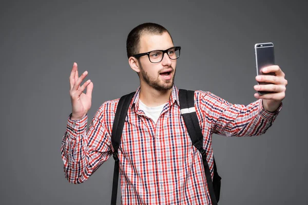 Glad ung man tar självporträtt fotografi via telefon över grå bakgrund. — Stockfoto