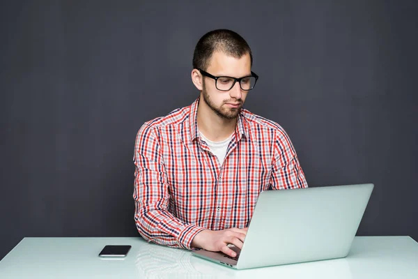 Retrato de hombre joven y ocupado trabajando en el ordenador portátil en el escritorio contra de la pared gris — Foto de Stock