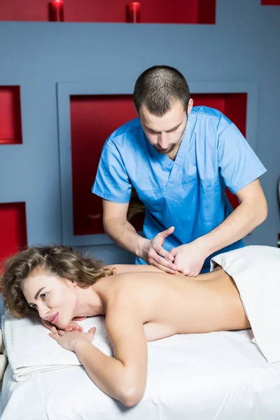 Terapeuta masajeando la espalda de una paciente joven en el spa de bienestar — Foto de Stock