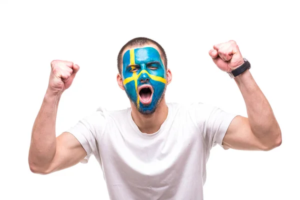 Knappe man supporter fan van Zweden nationale team met geschilderde vlag gezicht krijgen gelukkig overwinning schreeuwen in een camera. Emoties van de fans. — Stockfoto