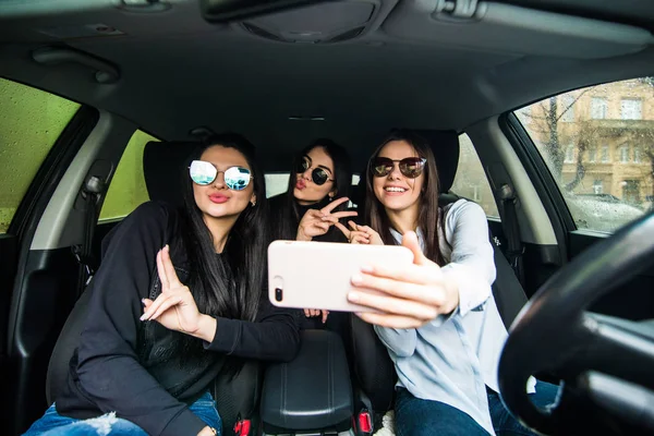 Selfie yapma ve arabaya birlikte otururken gülümseyen üç güzel genç neşeli kadın — Stok fotoğraf