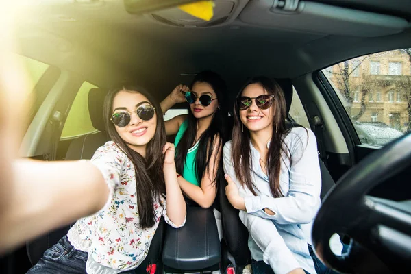 Три молодих веселих жінки роблять селфі і посміхаються, сидячи в машині разом — стокове фото