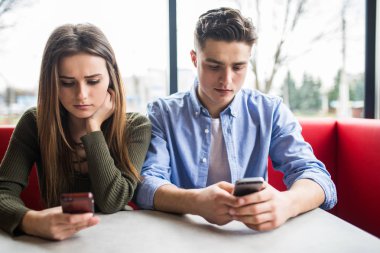 Young couple in cafe looking at their smartphones, social network concept clipart