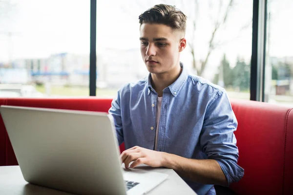 Jeune homme freelance bavarder sur téléphone mobile tout en étant assis devant ordinateur portable ouvert dans le café — Photo