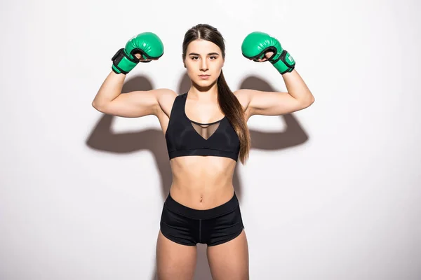 Lachende brunette fitness vrouw in bokshandschoenen weergeven van haar biceps tijdens het kijken naar de camera op witte achtergrond — Stockfoto