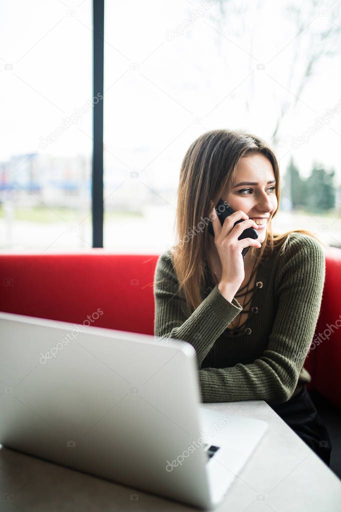 Happy woman using laptop and phone in cafe. Young beautiful girl sitting in a coffee shop and working on computer