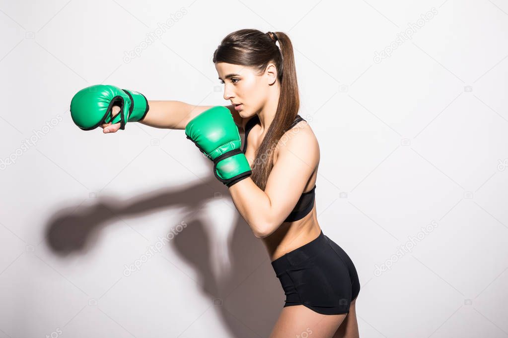 Young woman in sportswear and green boxing gloves smiles on a white isolated background