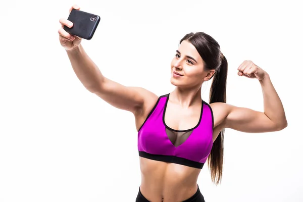 Feliz mulher esportiva fazendo foto selfie no smartphone e mostrando bíceps em um fundo branco — Fotografia de Stock