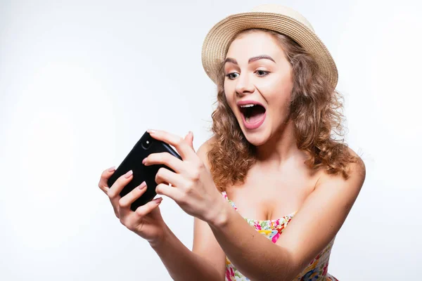 Fröhlich aufgeregtes Mädchen mit Sommerhut spielen Spiele oder machen Videoanruf auf dem Smartphone auf weißem Hintergrund — Stockfoto