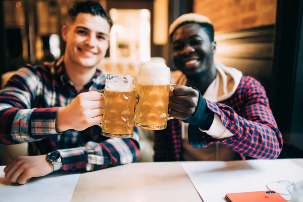 Dos mejores amigos o compañeros de universidad tomando cerveza en el pub. Afro hombre americano hablando con su amigo caucásico en el bar — Foto de Stock