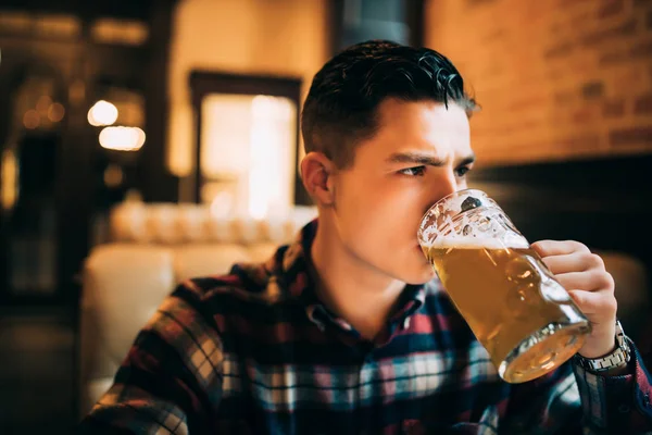 Um homem a beber cerveja. Jovem bonito bebendo cerveja enquanto estava sentado no balcão do bar — Fotografia de Stock