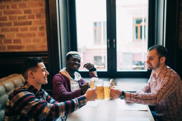 Grupo de jovens trabalhadores de escritório felizes clinking com cerveja no pub, saúde olhando uns para os outros, sorrindo . — Fotografia de Stock