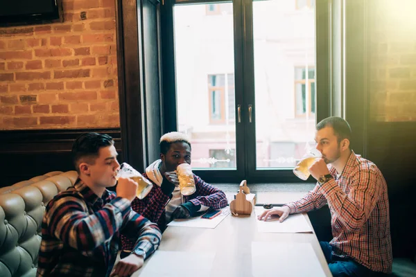 Amigos multirraciais estão falando e sorrindo enquanto descansam no pub — Fotografia de Stock