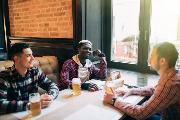 Grupo de jovens bonitos bebem com suas cervejas sentadas no pub relaxando juntos copyspace. pessoas lazer estilo de vida férias relaxamento recreação fim de semana beber — Fotografia de Stock