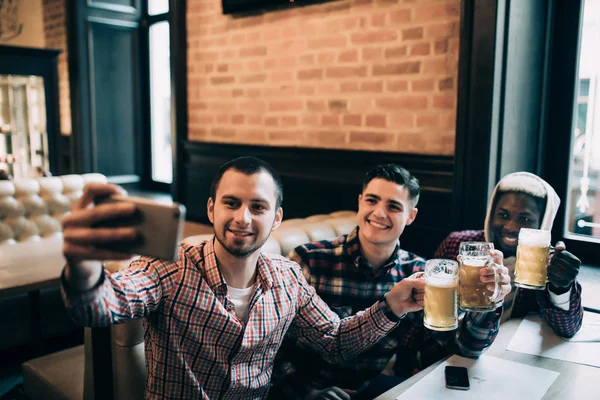 Glada gamla multietniska vänner har roligt tar selfie och dricka fatöl på pub. — Stockfoto
