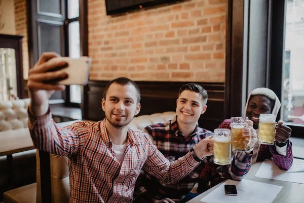 Glada gamla multietniska vänner har roligt tar selfie och dricka fatöl på pub. — Stockfoto